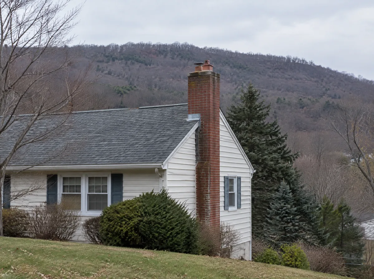 Technician working at a brick chimney on a roof with wooded hills behind