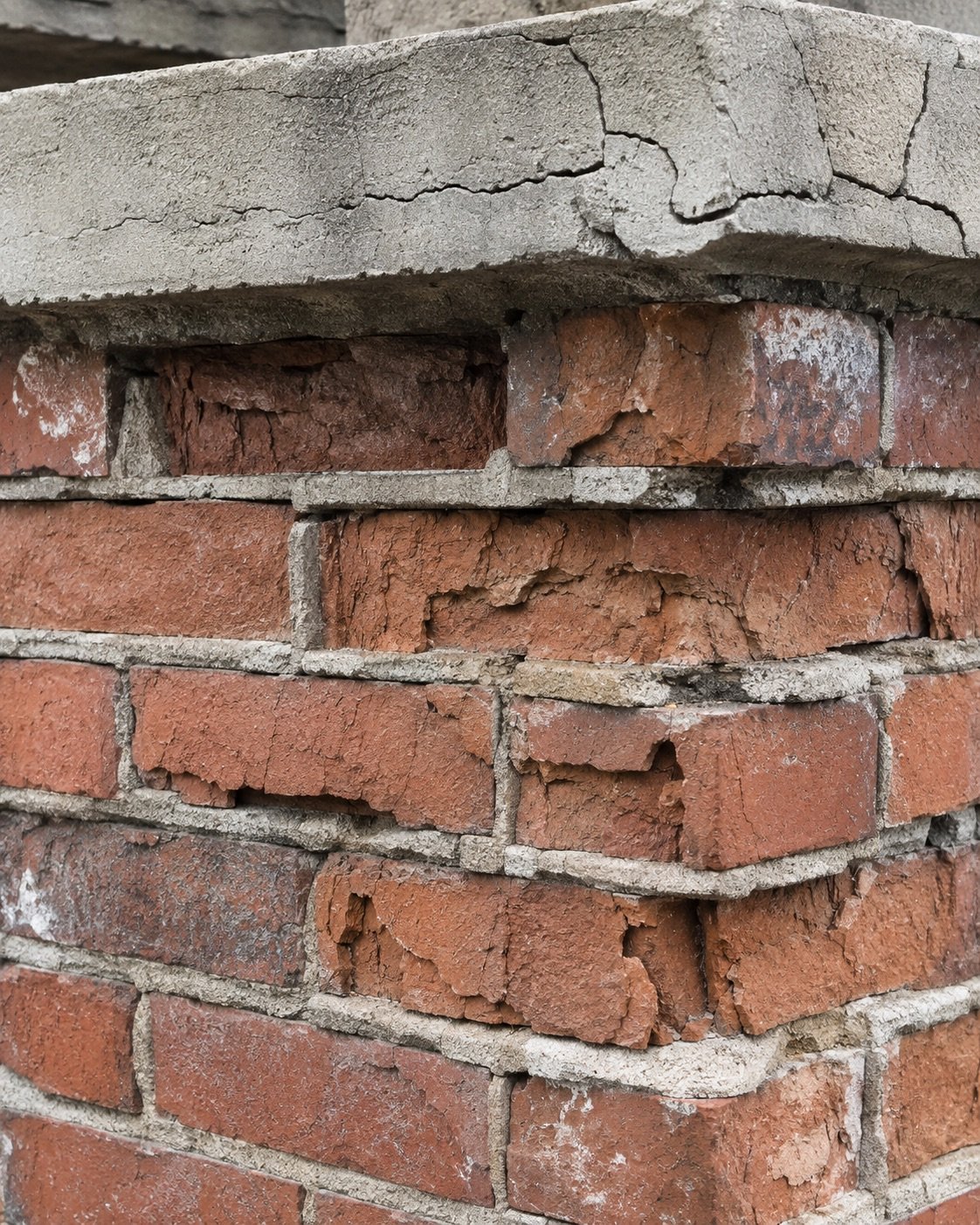 Spalled brick faces, open mortar joints and a cracked chimney crown caused by freeze-thaw damage