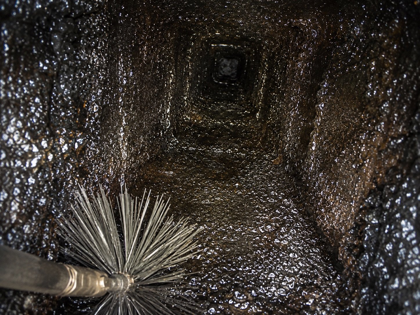 Glazed creosote coating the inside of a chimney flue with a wire brush in frame